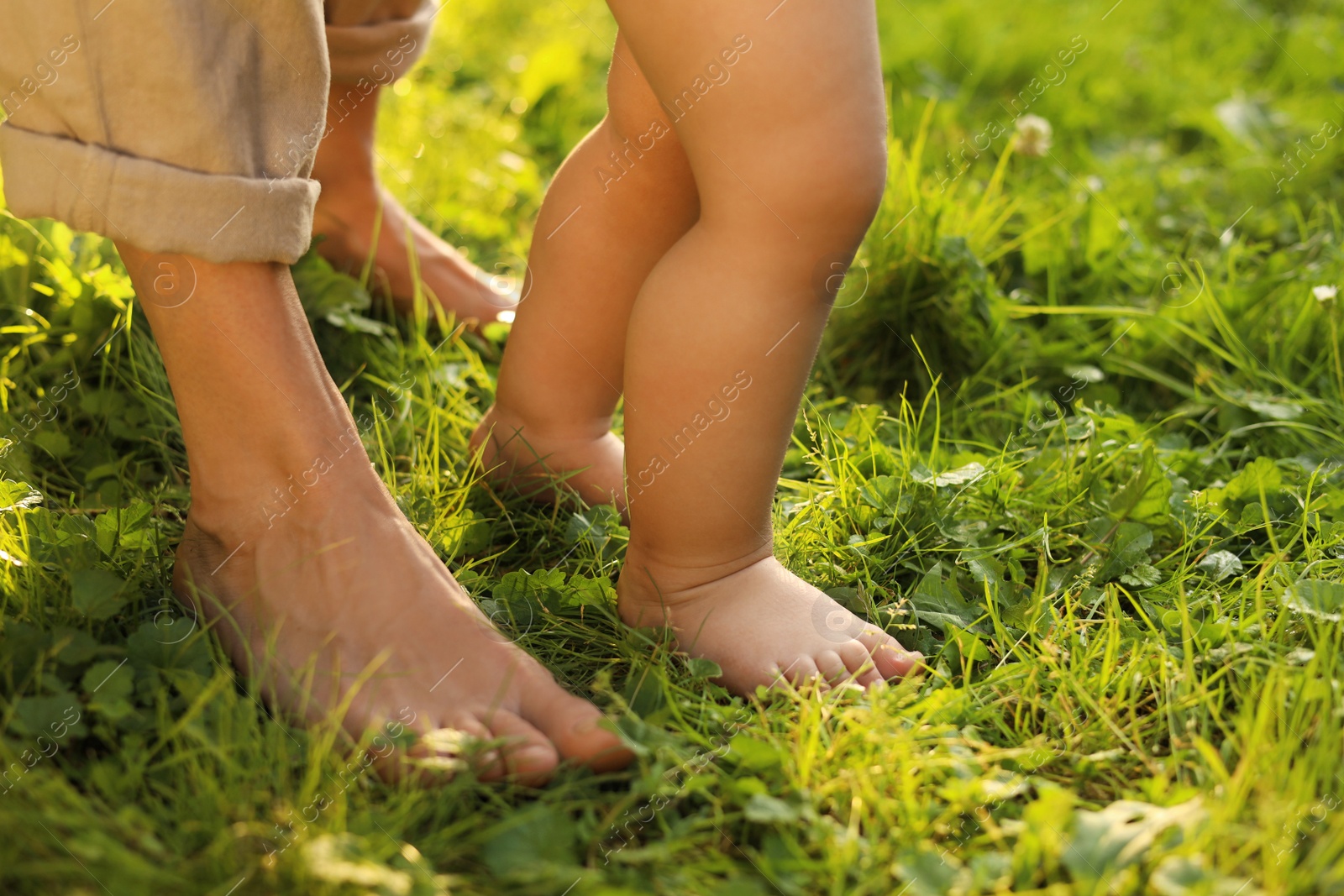 Photo of Woman with her child walking barefoot on green grass outdoors, closeup