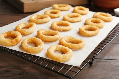 Photo of Cooling rack with tasty onion rings on wooden table