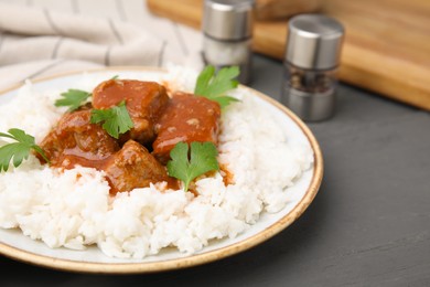 Photo of Delicious goulash served with rice on grey wooden table, closeup