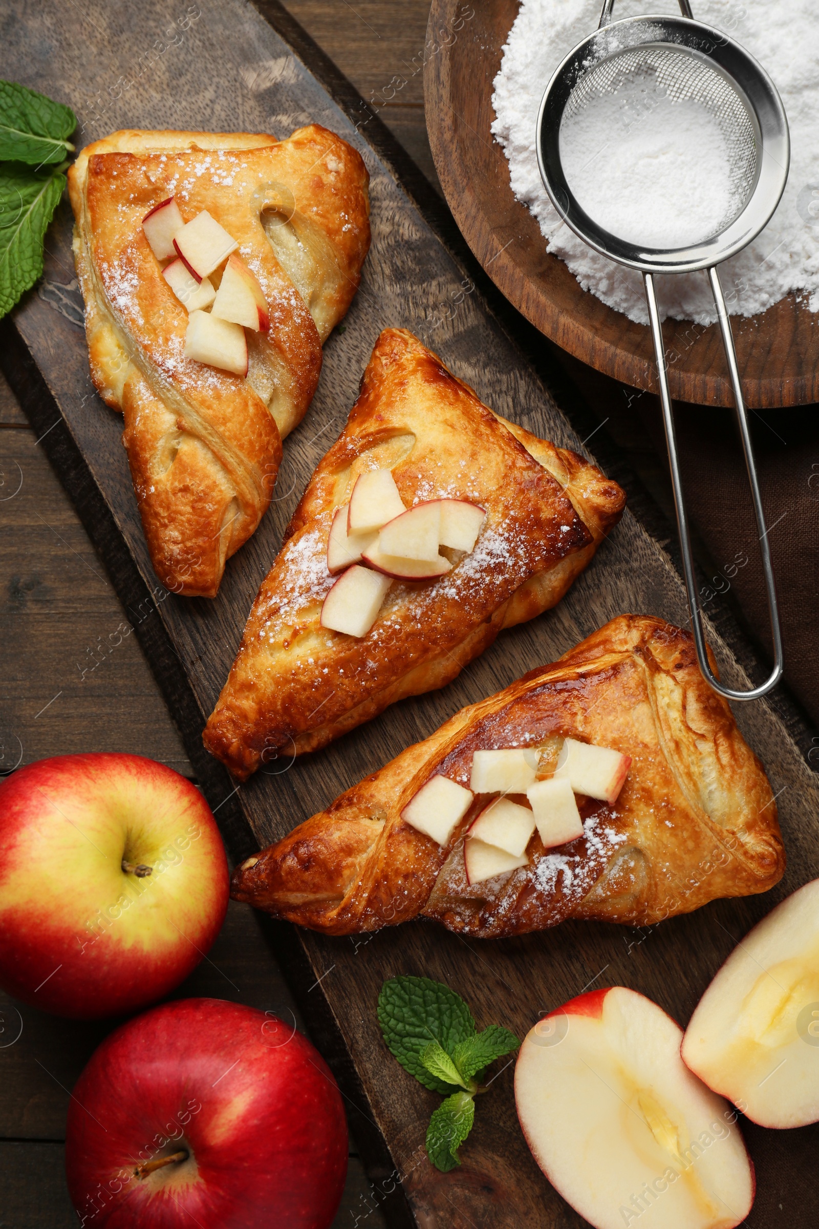 Photo of Fresh tasty puff pastry with sugar powder, mint and apples served on wooden table, flat lay