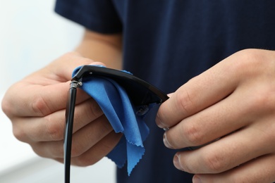 Photo of Man wiping sunglasses with microfiber cleaning cloth indoors, closeup