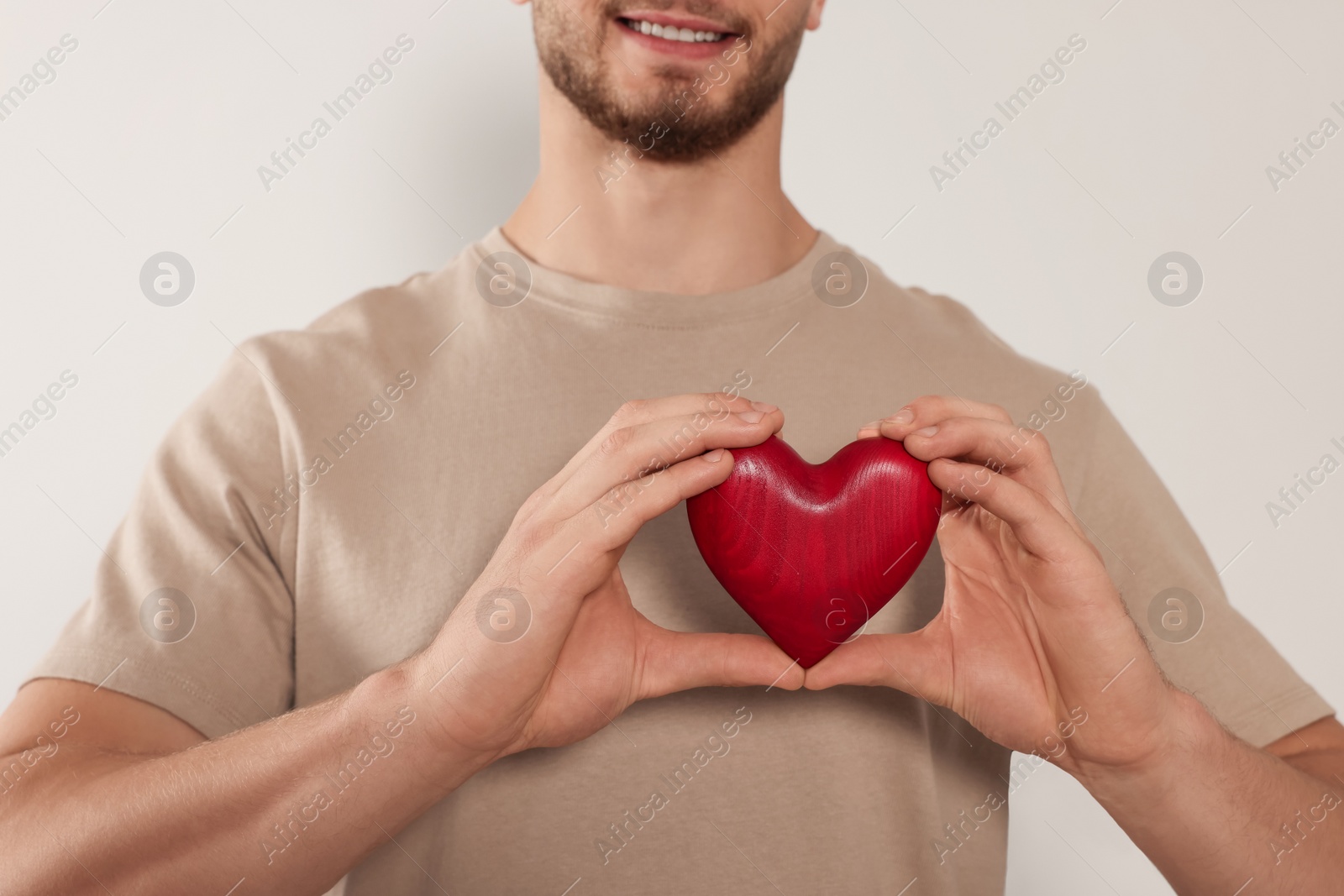 Photo of Happy volunteer holding red heart with hands on light background, closeup