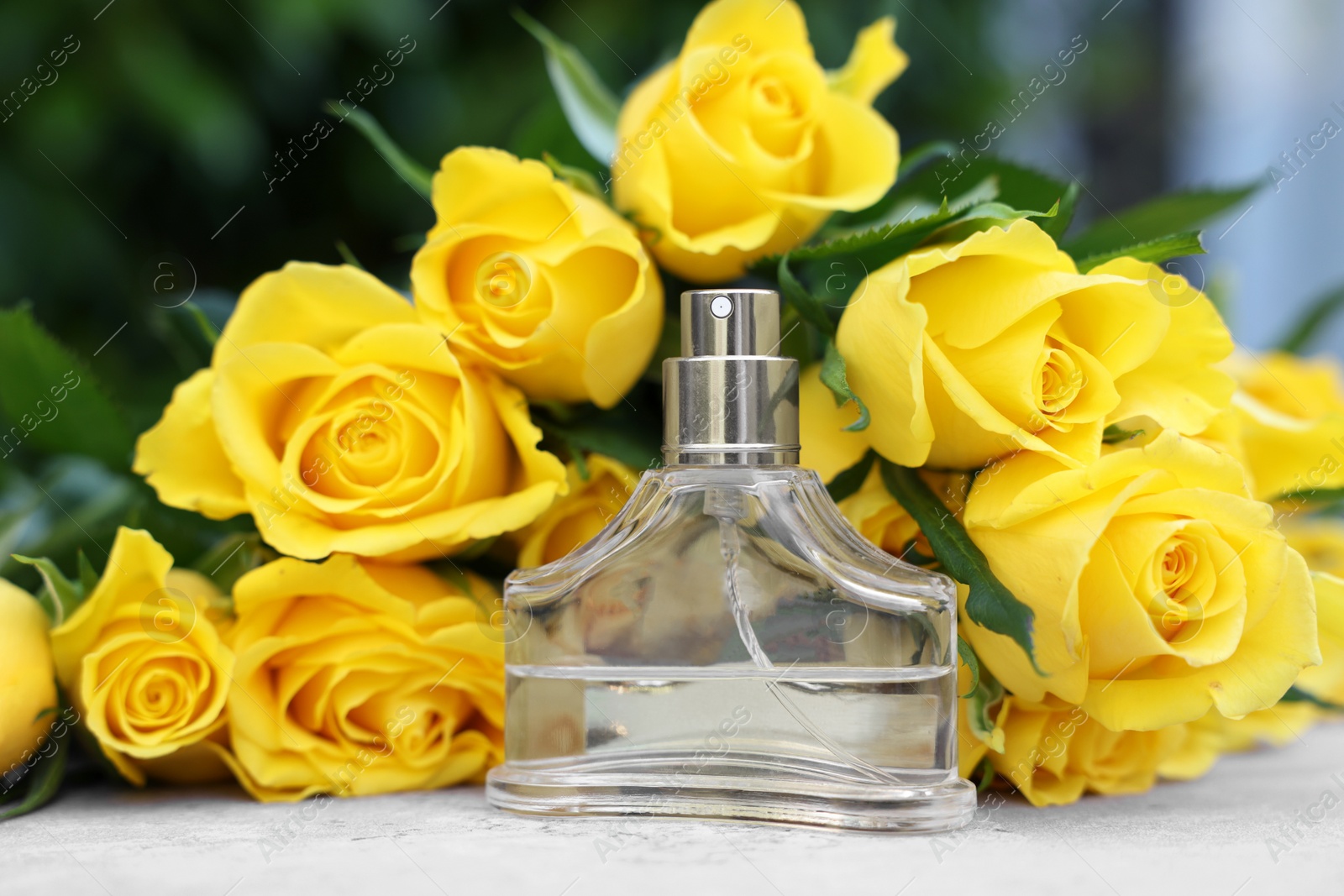 Photo of Perfume and beautiful bouquet of yellow roses on light table, closeup