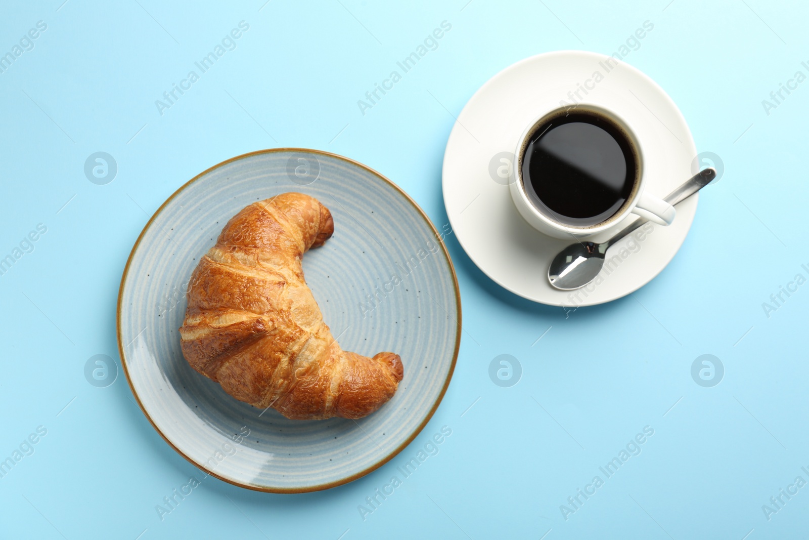 Photo of Delicious fresh croissant, cup of coffee and spoon on light blue table, flat lay