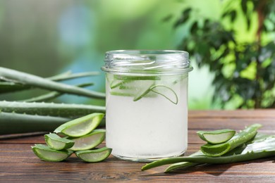 Photo of Fresh aloe juice in jar and leaves on wooden table outdoors, closeup