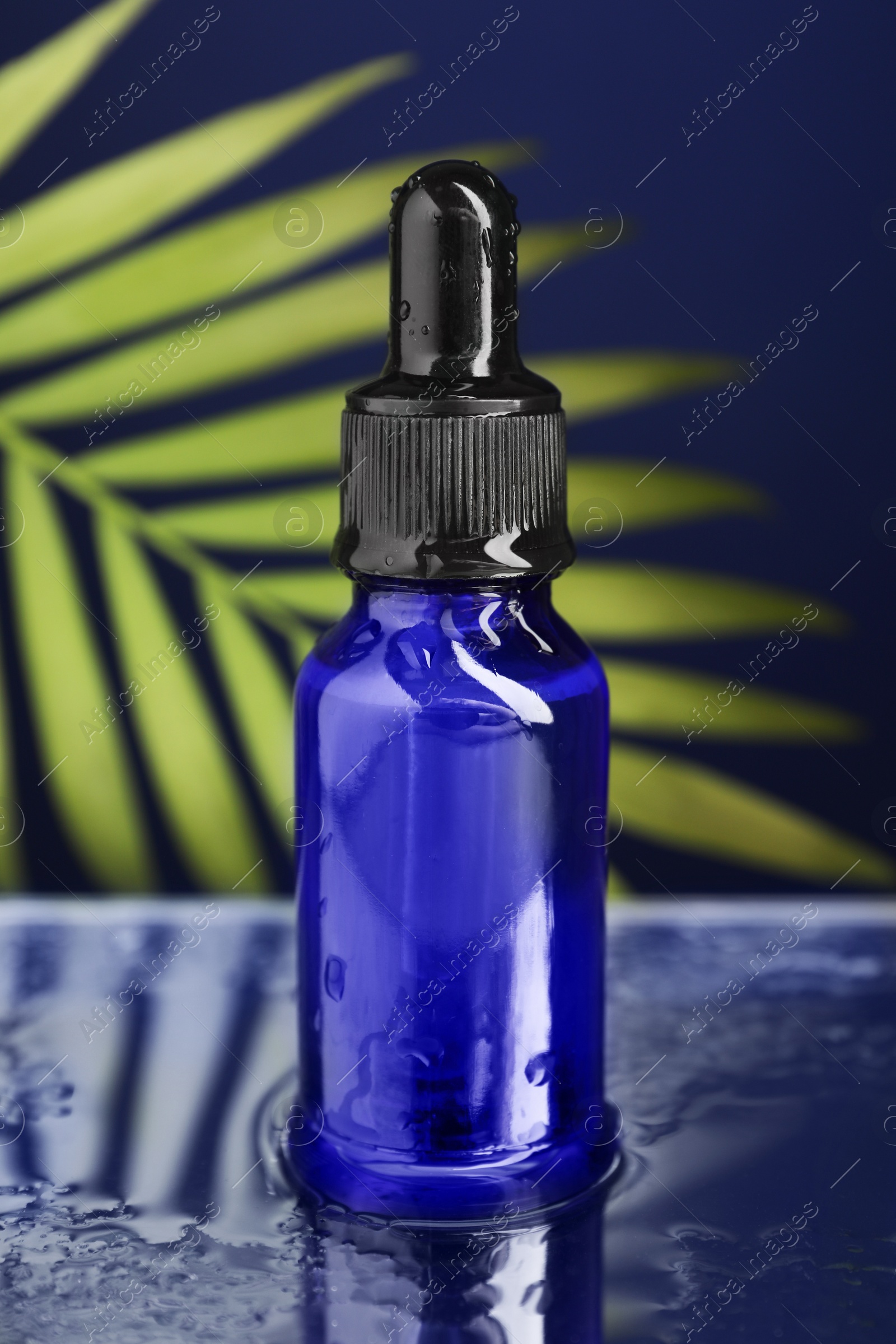 Photo of Bottle of face serum on wet surface against blue background, closeup