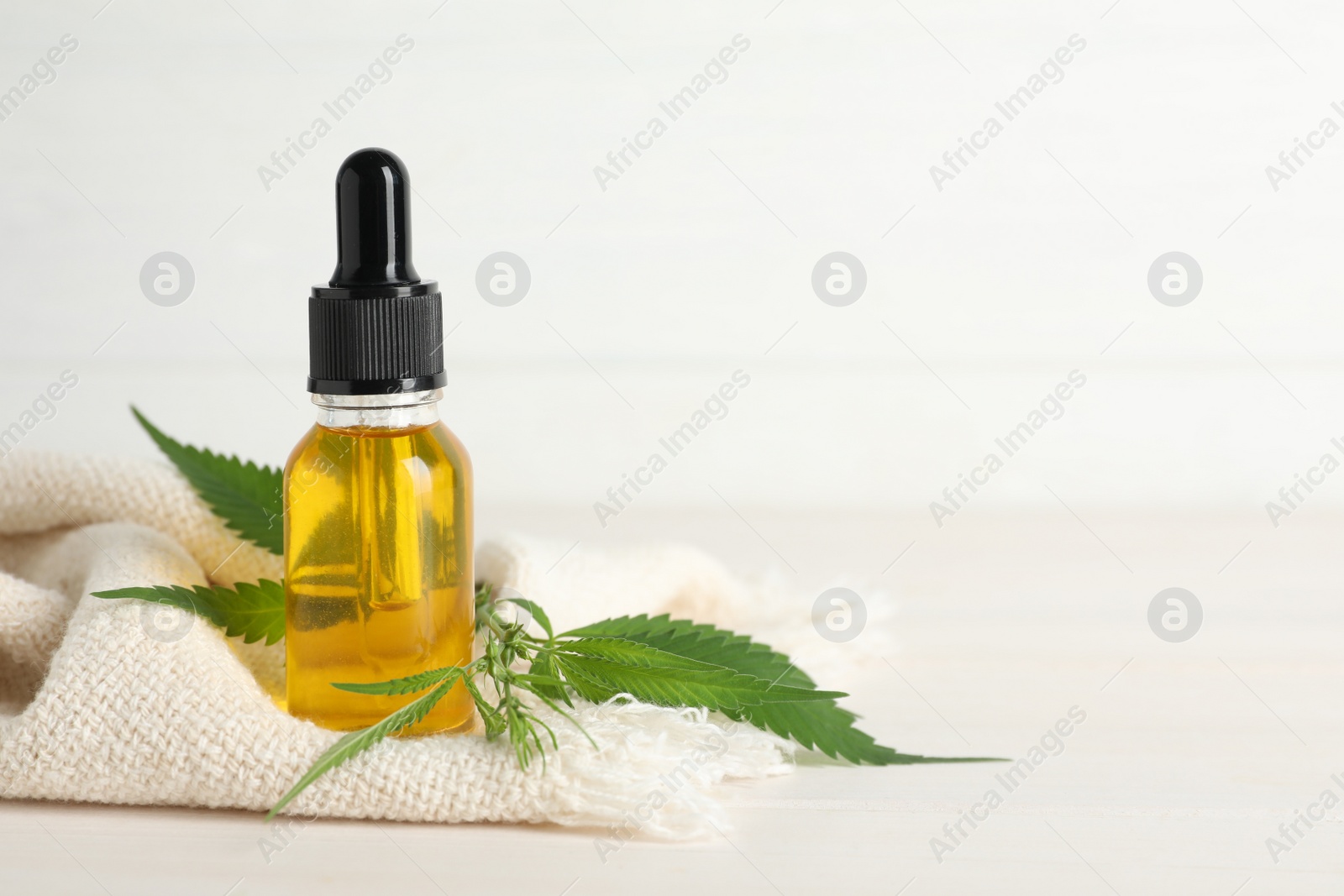 Photo of Bottle of CBD oil, hemp leaves and napkin on white table. Space for text