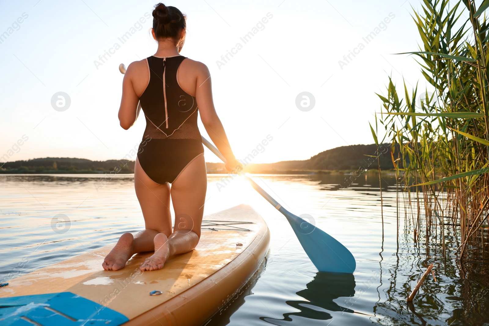 Photo of Woman paddle boarding on SUP board in river at sunset, back view