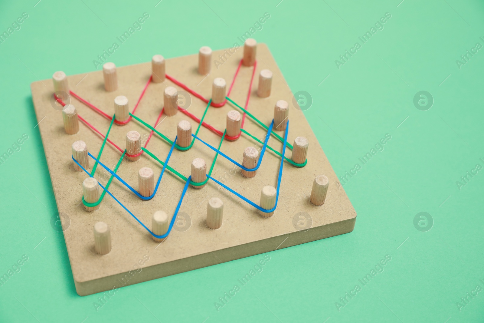 Photo of Wooden geoboard with rubber bands on green background. Educational toy for motor skills development