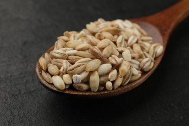 Photo of Wooden spoon with dry pearl barley on dark gray table, closeup