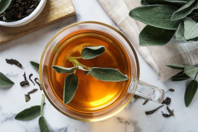 Photo of Cup of aromatic sage tea with fresh leaves on white marble table, flat lay