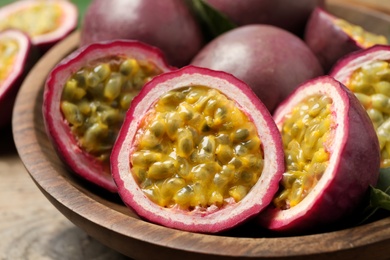 Photo of Cut and whole passion fruits (maracuyas) in wooden bowl, closeup