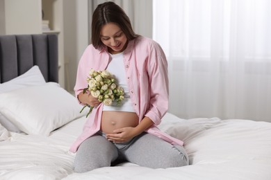 Beautiful pregnant woman with bouquet of roses in bedroom