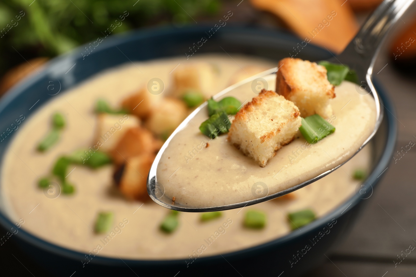 Photo of Spoon with fresh homemade mushroom soup over bowl, closeup