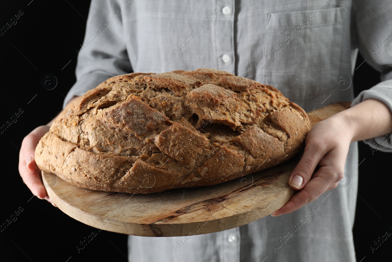 Photo of Woman holding freshly baked bread on black background, closeup