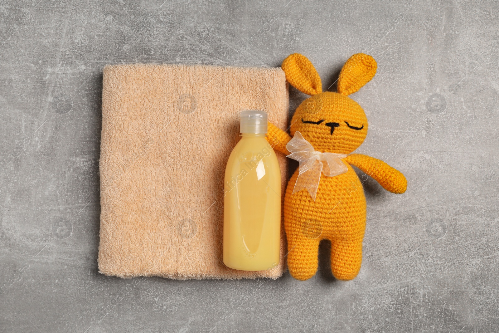 Photo of Bottle of laundry detergent, clean towel and rabbit toy on light grey table, flat lay