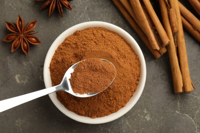 Photo of Bowl of cinnamon powder, sticks and star anise on grey table, flat lay