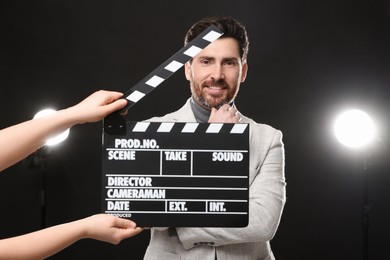 Photo of Actor performing while second assistant camera holding clapperboard on black background