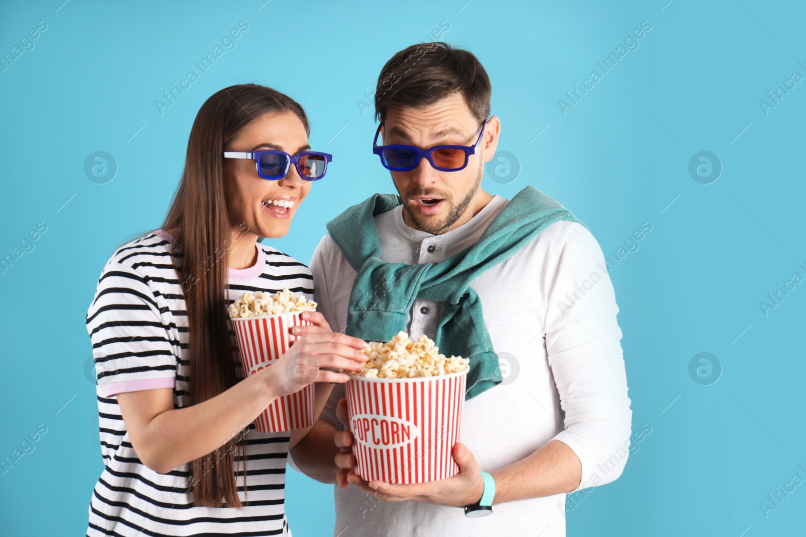 Photo of Young woman stealing popcorn from boyfriend on color background