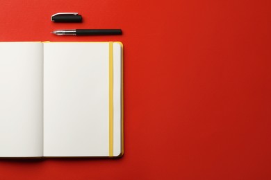 Notebook and pen on red background, flat lay. Space for text