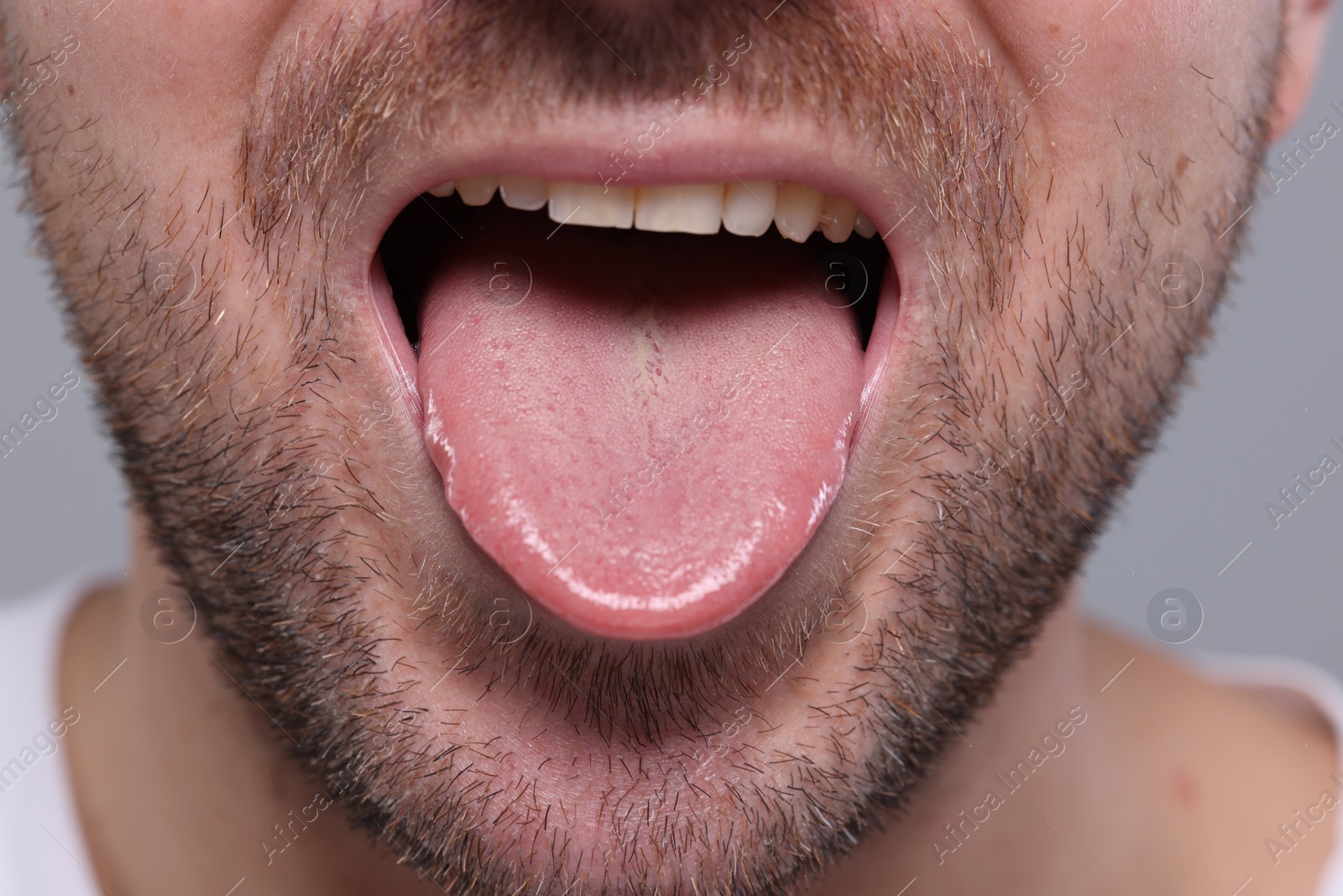 Photo of Closeup view of man showing his tongue on grey background