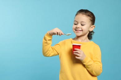 Girl with tasty yogurt on light blue background, space for text