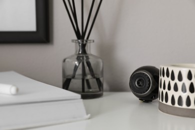 Photo of Small camera hidden among home stuff on white table indoors