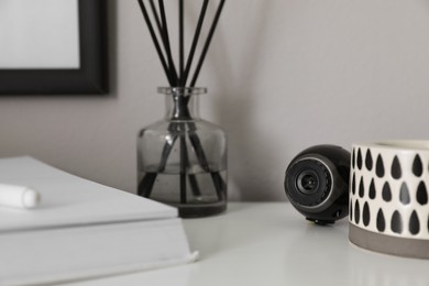 Small camera hidden among home stuff on white table indoors