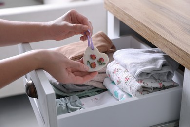 Photo of Woman putting heart shaped scented wax sachet into dresser drawer with folded clothes at home, closeup