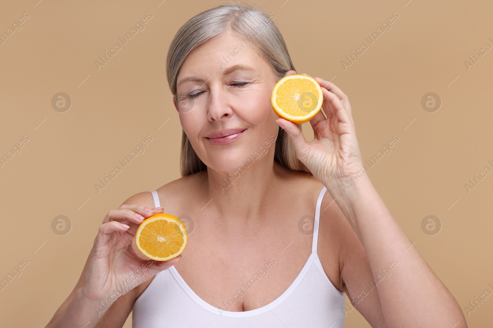 Photo of Beautiful woman with halves of orange rich in vitamin C on beige background