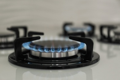 Photo of Gas burner with blue flame on modern stove, closeup