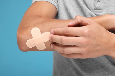 Photo of Man putting sticking plasters onto elbow on light blue background, closeup