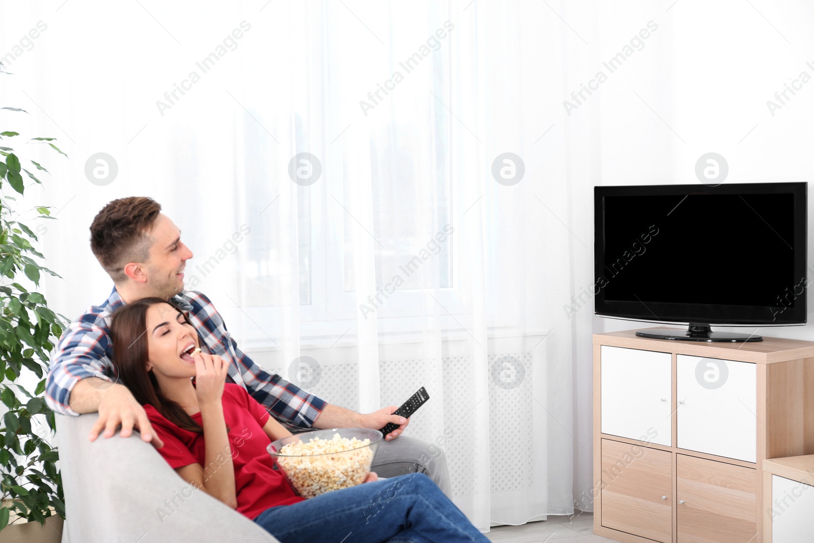 Photo of Happy young couple watching TV on sofa at home