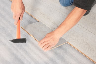 Photo of Professional worker using hammer during installation of new laminate flooring, closeup