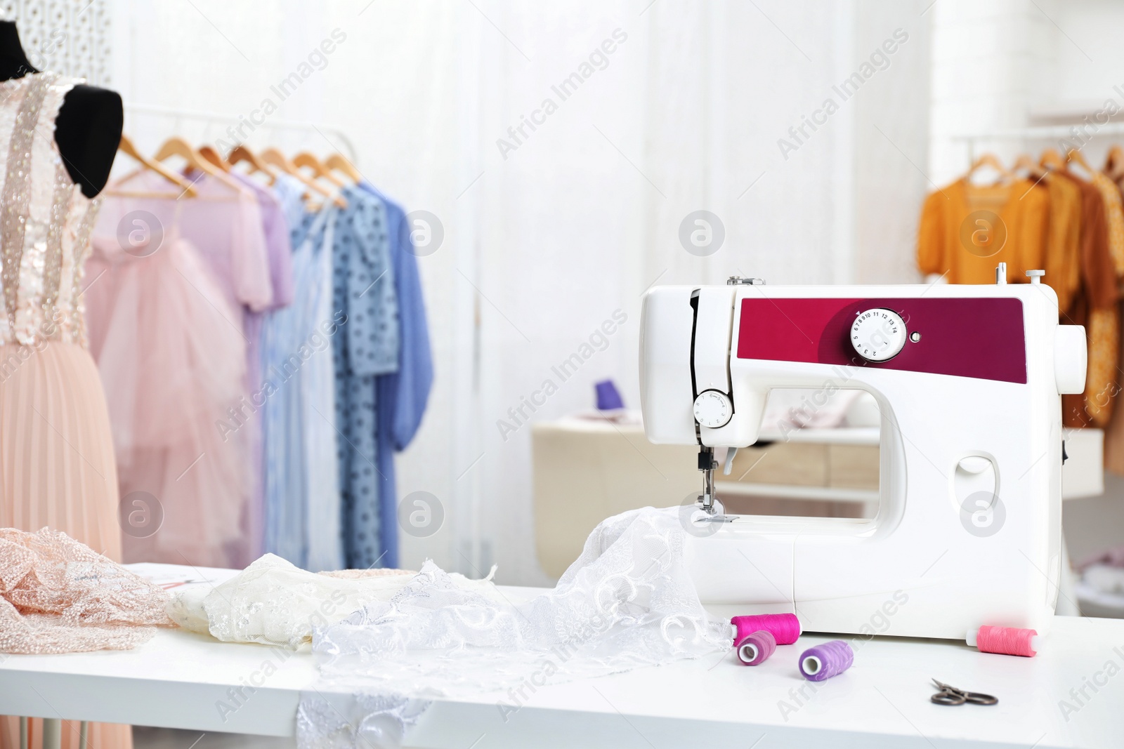 Photo of Modern sewing machine with fabric and bright threads on table in dressmaking workshop