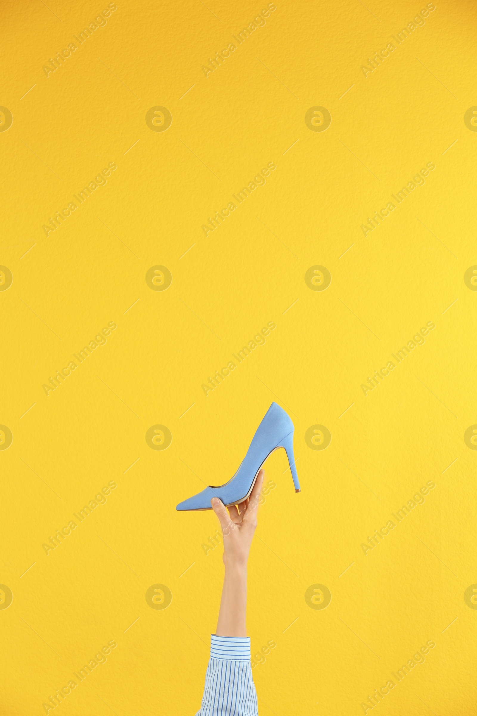 Photo of Woman holding classic high heeled shoe on yellow background, closeup. Space for text