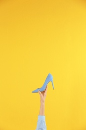 Photo of Woman holding classic high heeled shoe on yellow background, closeup. Space for text