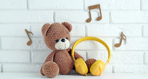 Photo of Baby songs. Toy bear and yellow headphones on white wooden table and notes