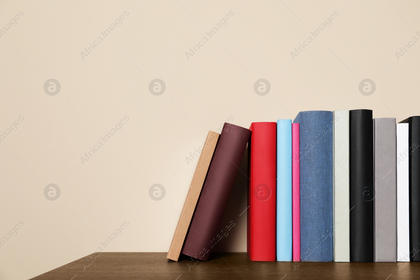 Photo of Different hardcover books on wooden table near beige wall. Space for text