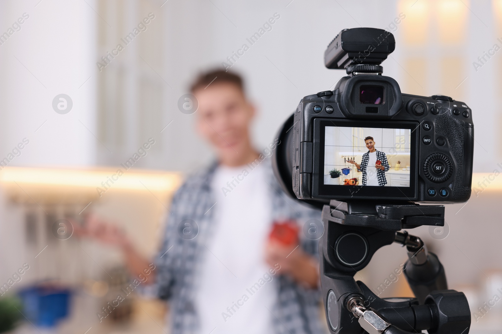 Photo of Food blogger recording video in kitchen, focus on camera