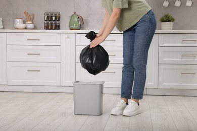 Photo of Woman taking garbage bag out of trash bin in kitchen, closeup