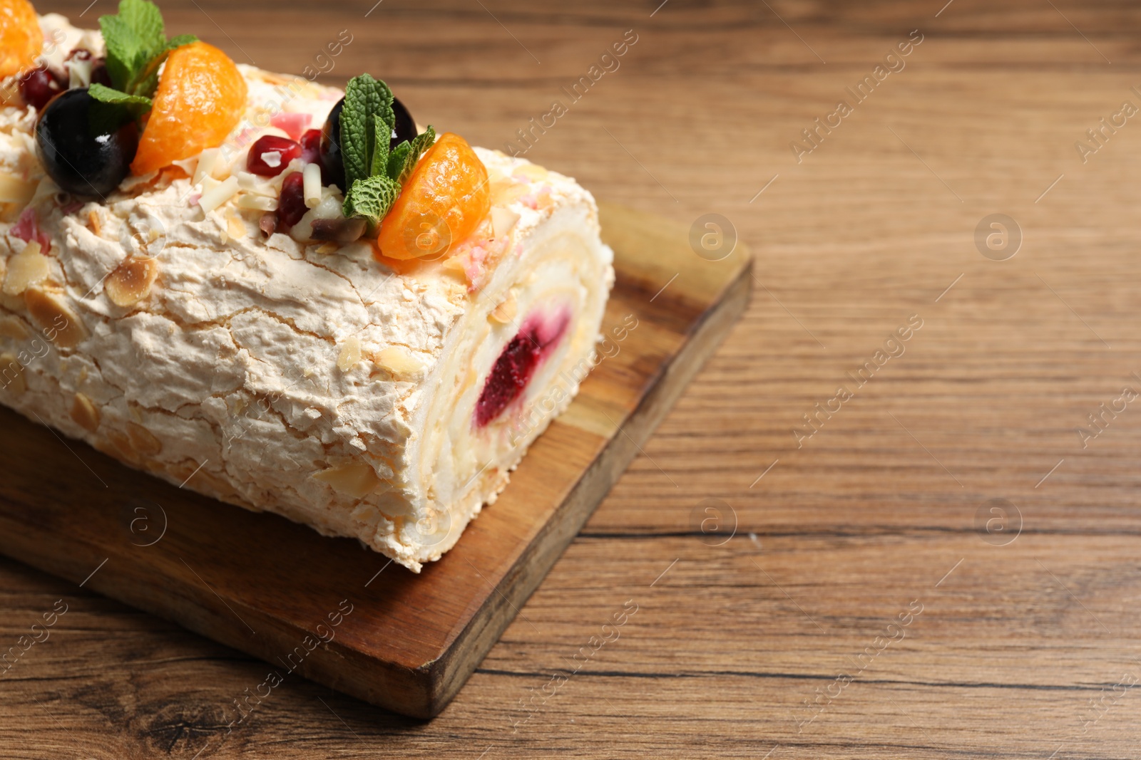 Photo of Tasty meringue roll with jam, tangerine slices and mint leaves on wooden table, closeup. Space for text