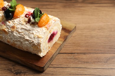 Tasty meringue roll with jam, tangerine slices and mint leaves on wooden table, closeup. Space for text