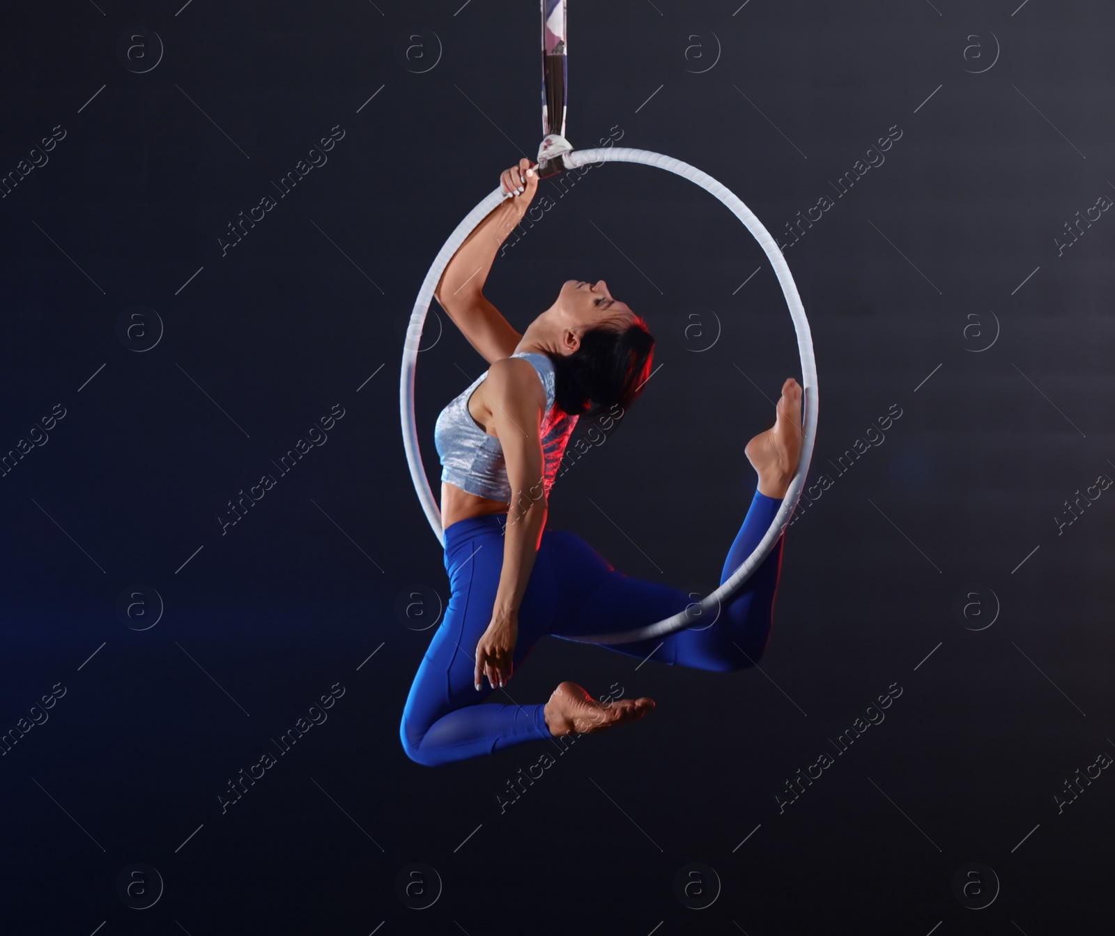 Photo of Young woman performing acrobatic element on aerial ring indoors