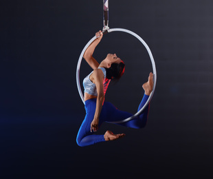 Young woman performing acrobatic element on aerial ring indoors
