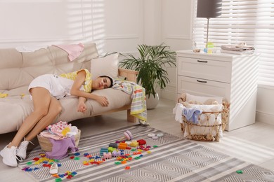 Photo of Tired young mother sleeping on sofa in messy living room