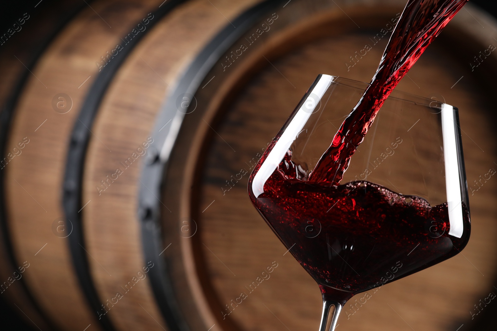 Photo of Pouring red wine into glass near wooden barrel, closeup. Space for text