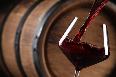 Pouring red wine into glass near wooden barrel, closeup. Space for text