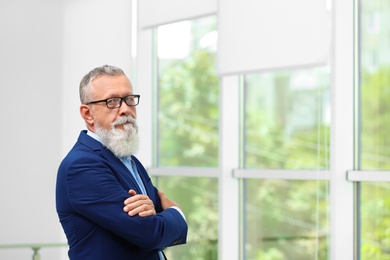 Portrait of handsome mature man in elegant suit with glasses indoors