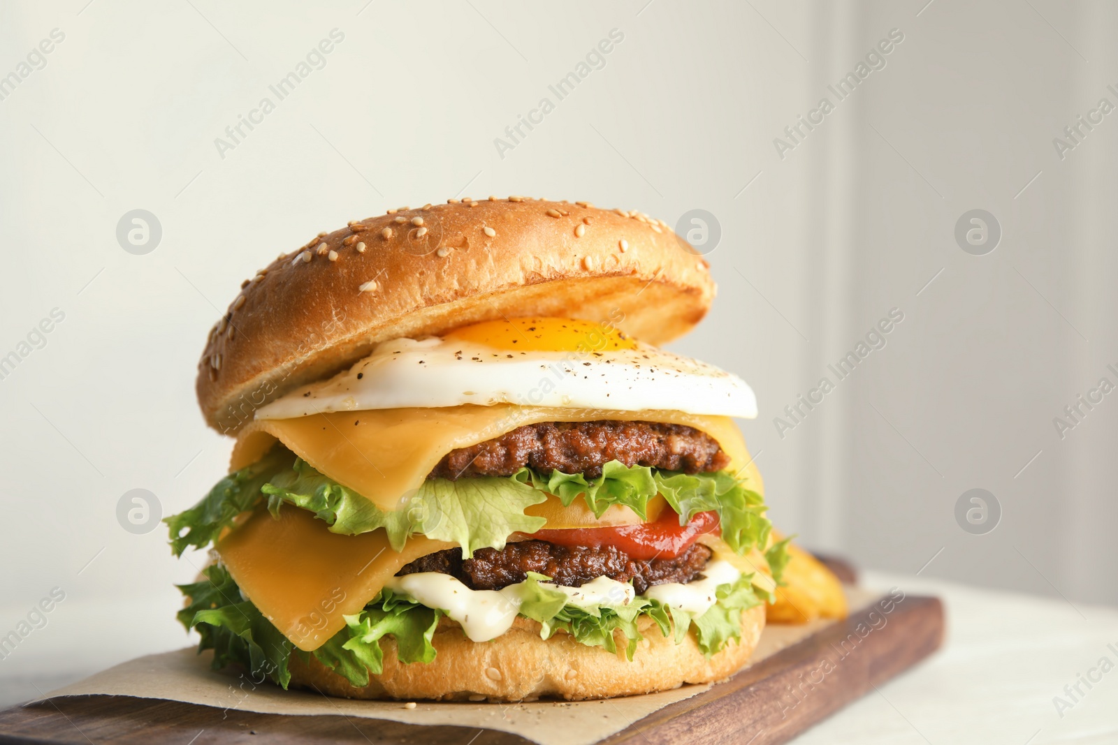 Photo of Tasty burger with fried egg on board against light background